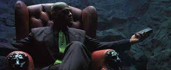 An image from the film The Matrix. Morpheus sits in a chair holding a remote control.